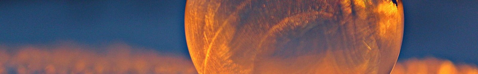Close-up shot of a frozen bubble with warm reflections resting on a snowy surface at twilight.